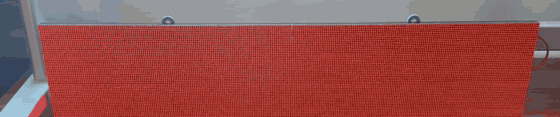 A bigsign panel on a wall cycling through full-frame red, green, blue, white, then black on real hardware, with the colors reflecting off the floor below.